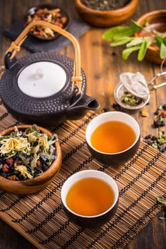Herbal and fruit tea concept with teapot and infuser and assorted herbal leaves on wooden background