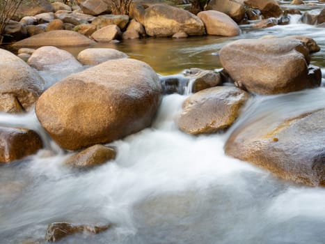 A long-exposure shot of a small creek flowing through a brown rock. And there are green trees as a backdrop. It is a specific focus.