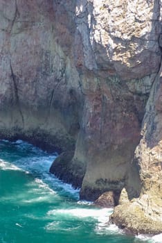 Waves crash against the cliffs in the Atlantic Ocean in southern Portugal. Tranquil vertical nature scene with texture, rough stone and swirling pale green water. Full frame in natural light with copy space.