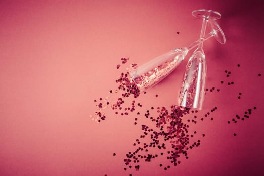 Two champagne glasses with splash of red heart shaped confetti on red background. Overhead view, copy space. Valentine's Day concept