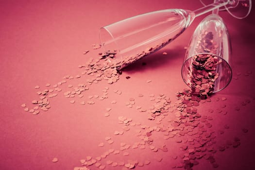 Two champagne glasses with splash of red heart shaped confetti on red background. Overhead view, copy space. Valentine's Day concept