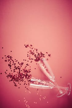 Two champagne glasses with splash of red heart shaped confetti on red background. Overhead view, copy space. Valentine's Day concept