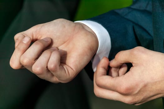 Adult male in a formal wear fashion suit adjusting and fastening his shirt sleeve button at a wedding, stock photo image