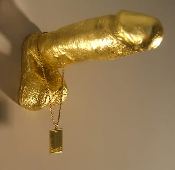 A gold penis figure hangs on the wall. Decoration in the style of sexuality.