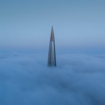 The top of the skyscraper above the fog. Fog over the city.