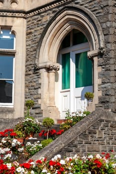 Old fashioned Victorian brick terraced house with a white wooden front door with arch and steps full of red pelargonium  geranium plants in containers and flower pots stock photo image