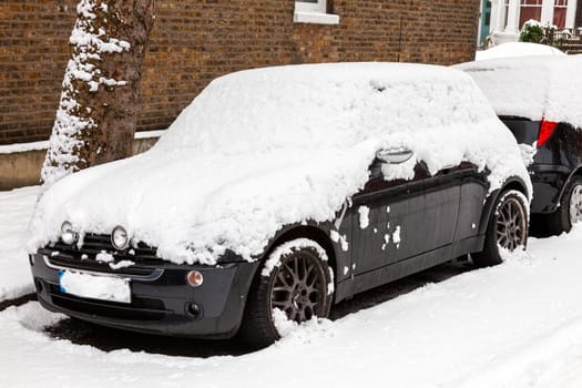Street winter cityscape with snow covered frozen cars after a blizzard snowfall in London England UK, stock photo image