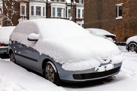 Street winter cityscape with snow covered frozen cars after a blizzard snowfall in London England UK, stock photo image