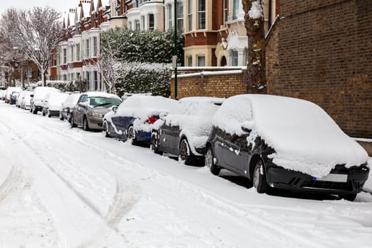 Street winter cityscape with snow terraced houses and frozen cars after a blizzard snowfall in London England UK, stock photo image with copy space