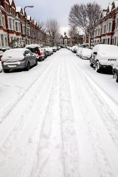 Street winter cityscape with snow terraced houses and frozen cars after a blizzard snowfall in London England UK, stock photo image with copy space