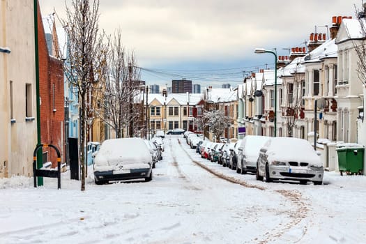 Street winter cityscape with snow terraced houses and frozen cars after a blizzard snowfall in London England UK, stock photo image with copy space