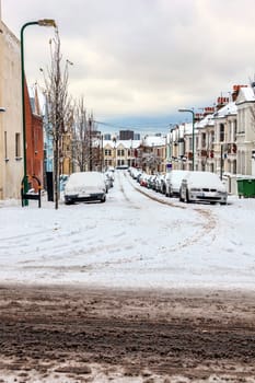 Street winter cityscape with snow terraced houses and frozen cars after a blizzard snowfall in London England UK, stock photo image with copy space