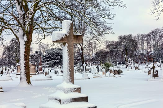 Cemetery winter cityscape with snow covered graveyard tombstone cross after a blizzard snowfall, stock photo image