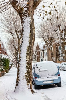 Street winter cityscape with snow terraced houses and frozen cars after a blizzard snowfall in London England UK, stock photo image with copy space