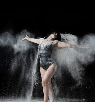 beautiful Caucasian woman throws white flour with her hands in different directions on a black background, graceful dance