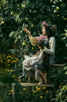 A girl on a wooden bench with a bouquet of flowers and a wreath on her head.