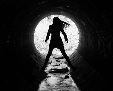 The silhouette of a young woman in the coc of the tunnel. A sewer tunnel under the road.
