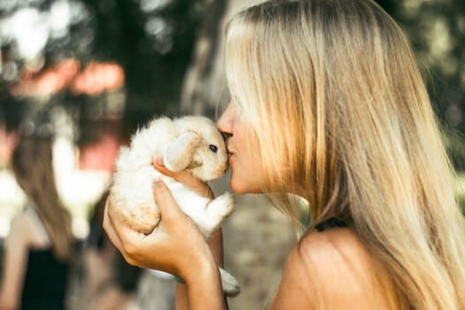 Blonde girl kisses a rabbit. Cute rabbit in his hands