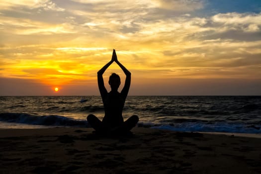 The figure of a girl on the background of the sea and sunset in a yoga pose on one leg.