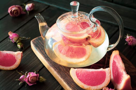 Pink grapefruit herbal tea with ginger and honey in a glass teapot on dark background