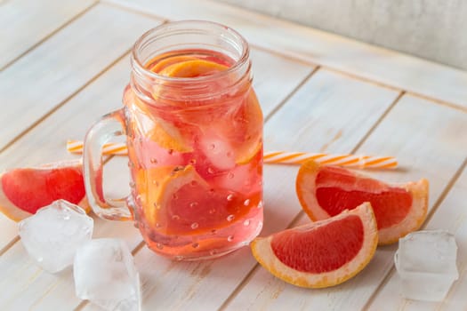 Fresh pink grapefruit cocktail. Fresh summer cocktail with grapefruit and ice cubes. Glass of grapefruit mojito, white wooden background