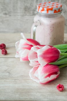 Pink raspberry smoothie in a mason jar with fresh berries and pink tulips on a rustic wood background, vertical image