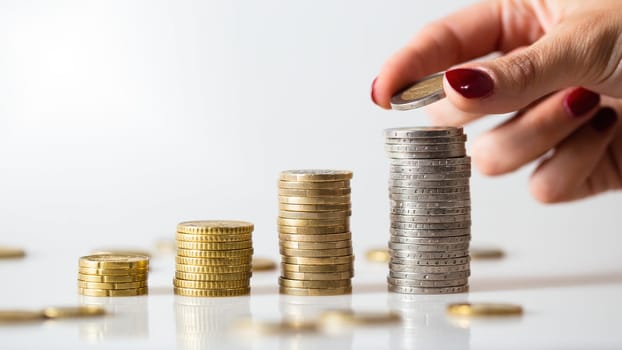 Saving money in piles of coins on white background. Concept of investment and raising value of finances. Woman holding euro in hand and building columns from it.
