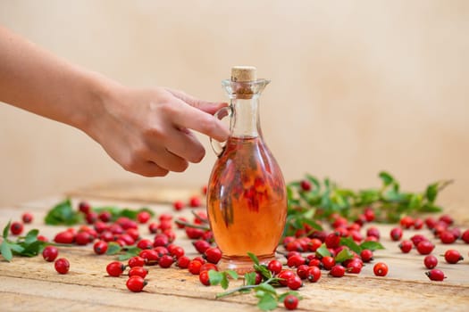 Hand putting down a flask with pink rosehip oil on a brown wooden table. Arm with fingers holding glass vial with pink lotion made out of wild berries.