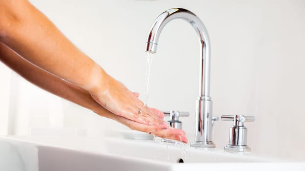 Woman washing hands under running water in white bathroom. palm zoom in. Lady cleaning skin under in washbasin. Protection with hygiene care against the viruses.