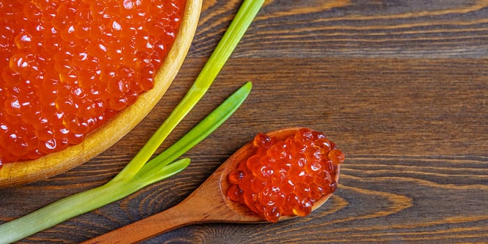 Red caviar in a wooden cup on a wooden background with a spoon. Place for advertisement, logo, label, mockup, mock-up.
