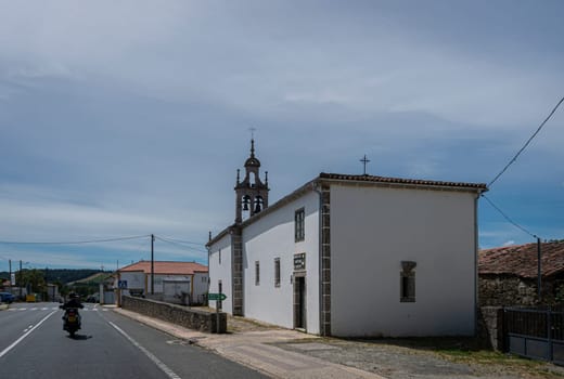 A motorbike riding past a church in the village of Boente, Spain