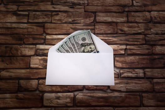 White envelope with five hundred dollar bills on the background of a dark brick wall.