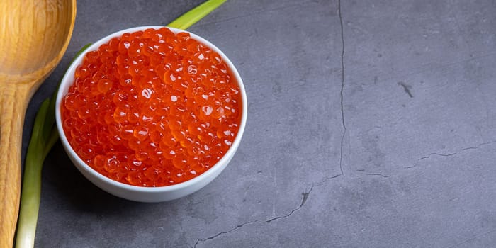 Red caviar in a wooden cup on a grey background with a spoon. Place for advertisement, logo, label, mockup, mock-up.