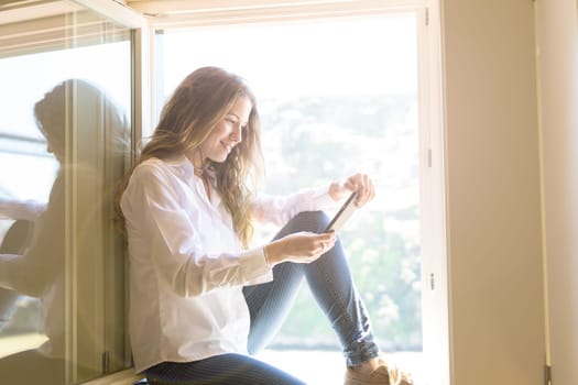 Young woman catching some sun at the balcony while using her new smartphone