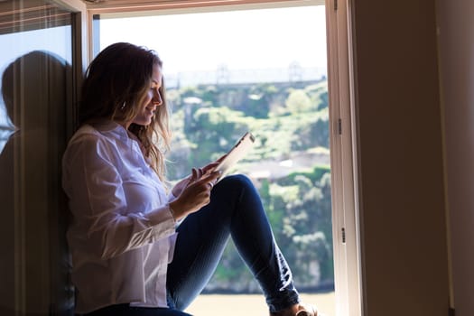 Young woman catching some sun at the balcony and checking the social networks