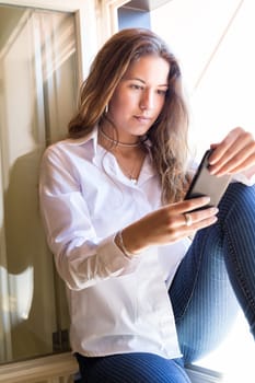 Young woman catching some sun at the balcony while using her new smartphone