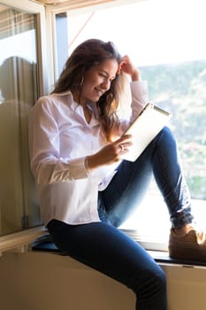 Young woman catching some sun at the balcony and checking the social networks