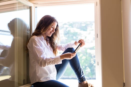 Young woman catching some sun at the balcony while using her new smartphone