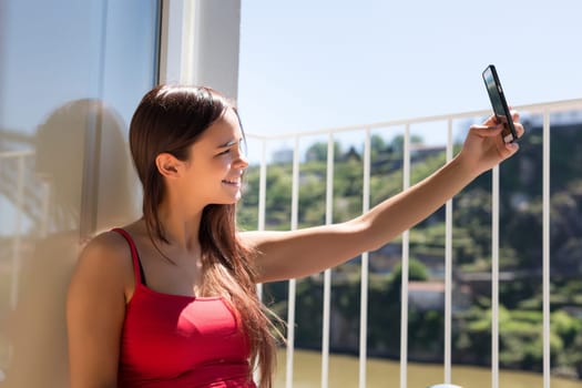 Young woman catching some sun at the balcony while using her new smartphone