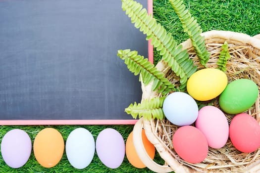 Close up Colorful easter eggs on green grass and blackboard mockup with copy space