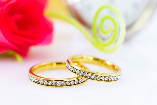 Two golden wedding rings and branch flowers on white background