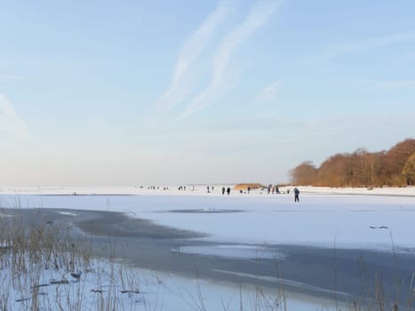 people walk and go fishing on the frozen lake in winter on a sunny day