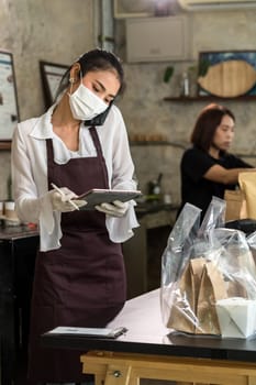 Asian waitress take order from mobile phone for takeout and curbside pickup orders while city lockdown. They wear protective face mask to prevent from infection of coronavirus COVID-19 pandemic.