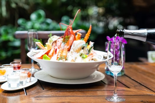 Waiter pouring white wine into wine glass and serving to customer in restaurant with big bowl seafood on ice in background. Restaurant gastronomy food and drink consumerism concept.
