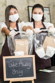 Close up waitress wear protective face mask smile and hold shopping bag for take away or takeout food. This essential service is very popular while city lockdown from coronavirus COVID-19 Pandemic