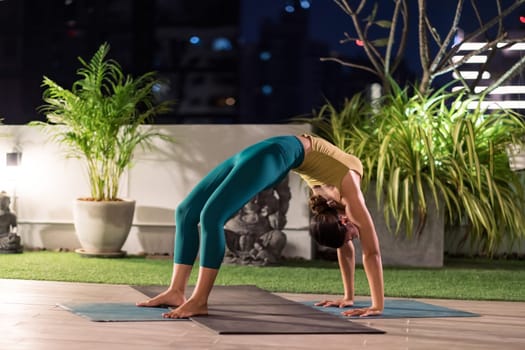 Asian female woman in sportswear bra pants practicing yoga during city lockdown alone in her apratment with background of cityscape illumination at night. Work out fitness healthy lifestyle concept.