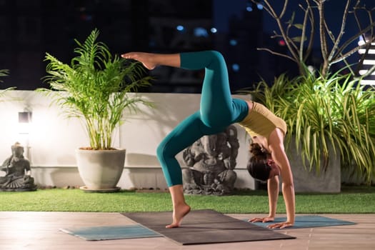 Asian female woman in sportswear bra pants practicing yoga during city lockdown alone in her apratment with background of cityscape illumination at night. Work out fitness healthy lifestyle concept.