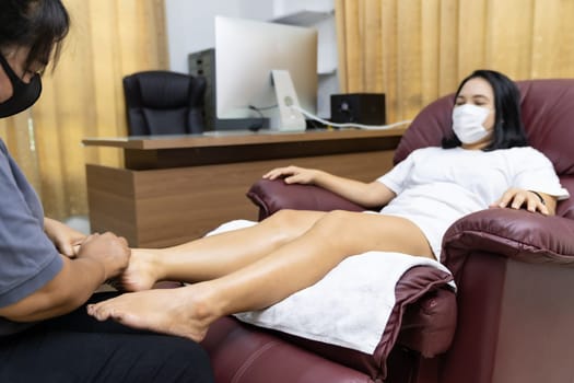 Quarantine asian woman do foot massage at home with face mask while city lockdown for social distance due to coronavirus pandemic. Massage is one of service business that shutdown while city lockdown.