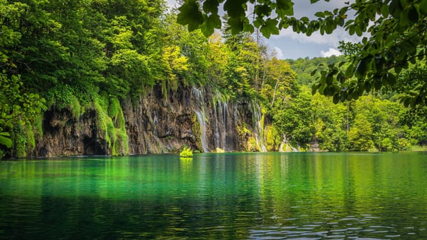 Beautiful waterfall illuminated by sunlight with reflections in lake. Green lush forest, Plitvice Lakes National Park UNESCO World Heritage in Croatia