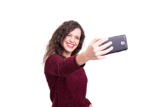 Happy young woman taking self portrait photography through smart phone over white background.